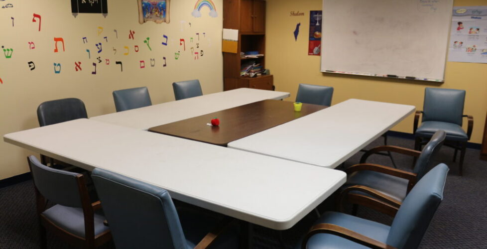 Photograph of small classroom; tables surrounded by chairs, and a whiteboard.