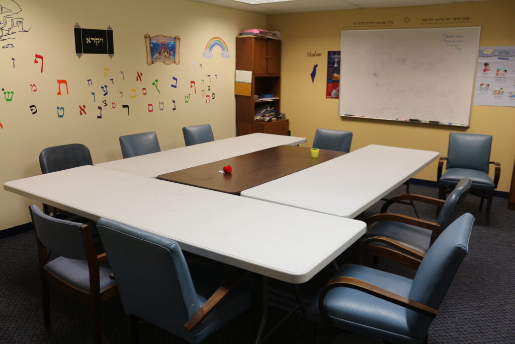 Photograph of small classroom; tables surrounded by chairs, and a whiteboard.