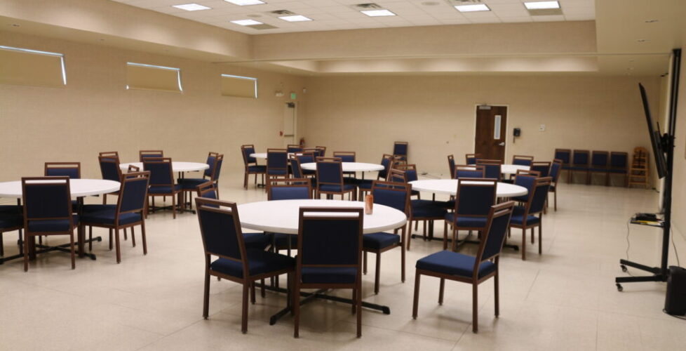 Photograph of multipurpose room. There are several tables each surrounded with chairs.