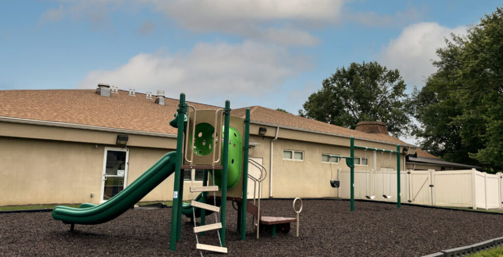 A photograph of the temple playground; includes a playset with slide and a separate swing set.