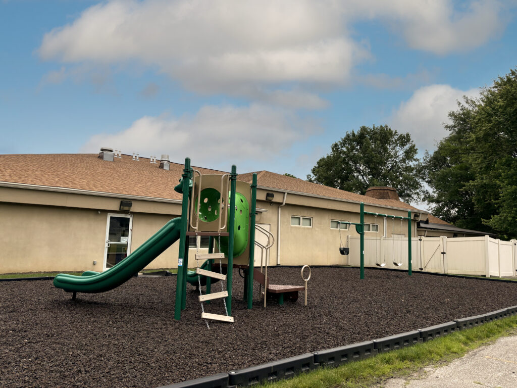 A photograph of the temple playground; includes a playset with slide and a separate swing set.